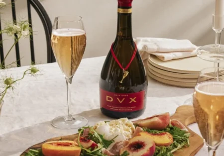A bottle and two glasses of Mumm Napa DVX Rosé with a platter of Grilled Peach And Prosciutto Salad