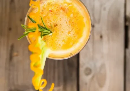 A glass of blood orange punch, photographed from above, garnished with a twist of orange peel and sprig of sage
