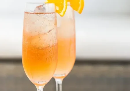 Two glasses of ginger spritzer in champagne flutes, garnished with small wedges of orange