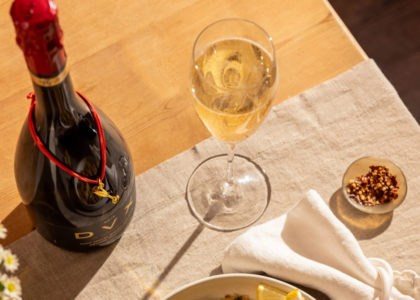 A glass of sparkling wine next to an unopened bottle of Mumm Napa DVX