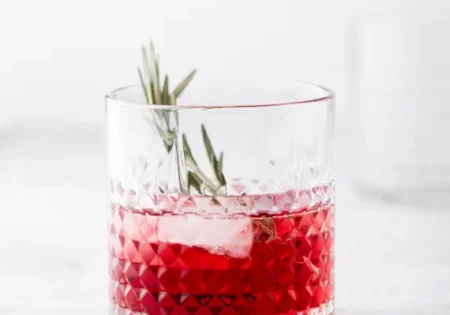 a glass of rosé cranberry spritz in a chunky glass tumbler with a sage sprig garnish