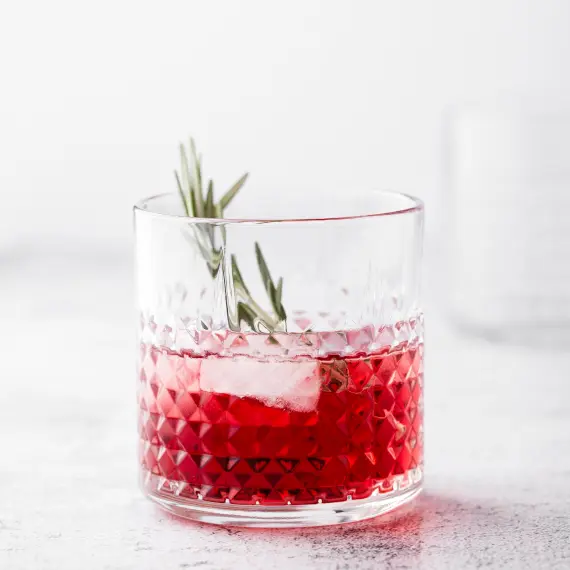 a glass of rosé cranberry spritz in a chunky glass tumbler with a sage sprig garnish