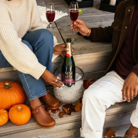 A couple sit on wooden steps next to pumpkins, with a bottle of Mumm Napa sparkling pinot noir in a clear ice bucket between them