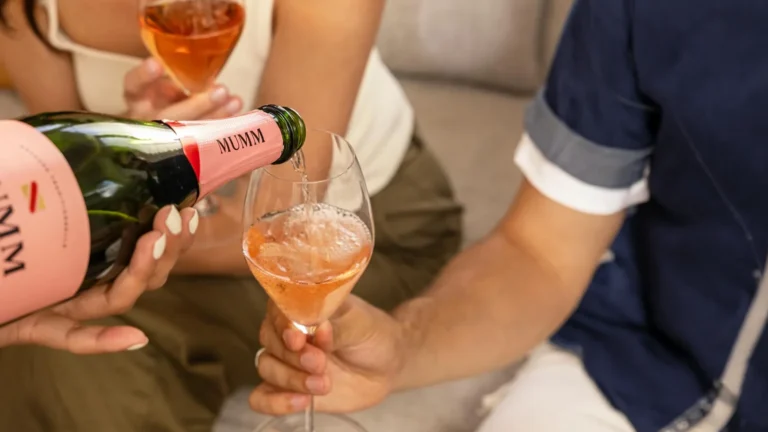 An unseen person pours a glass of Mumm Napa Brut Rosé sparkling wine for a party guest