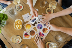 People around a table with glasses of wine and chips search through cards showing different sparkling wine flavors