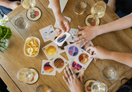 People around a table with glasses of wine and chips search through cards showing different sparkling wine flavors