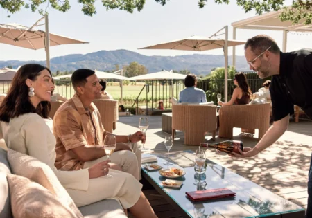 A server pours a glass of Mumm Napa DVX sparkling wine for a couple sitting outside on the Oak Terrace of the Mumm Napa winery
