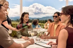 A group sits around a table at Mumm Napa's outdoor tasting patio while a server pours a glass of Mumm Napa