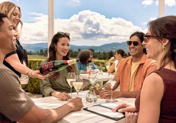 A group sits around a table at Mumm Napa's outdoor tasting patio while a server pours a glass of Mumm Napa